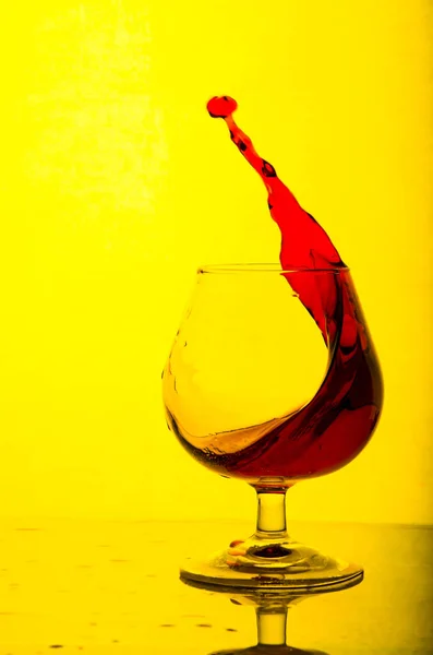 Splash of red wine in a glass. Yellow background