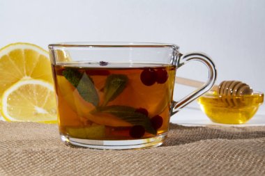 Bardak bardakta çay, limon böğürtlen ve nane şekeri, limon ve balın arka planında cam bir kasede.