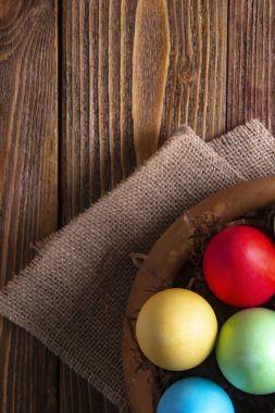 Easter Composition. Colored eggs in a wooden plate on a linen napkin on a wooden table.