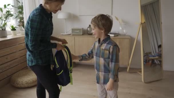 Mutter trägt Kind zur Schule und gibt ihm einen Rucksack. — Stockvideo