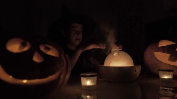 Niño de 9 años juega al mago en Halloween. Con una lámpara mágica y una calabaza en la mesa por la noche . — Vídeo de stock