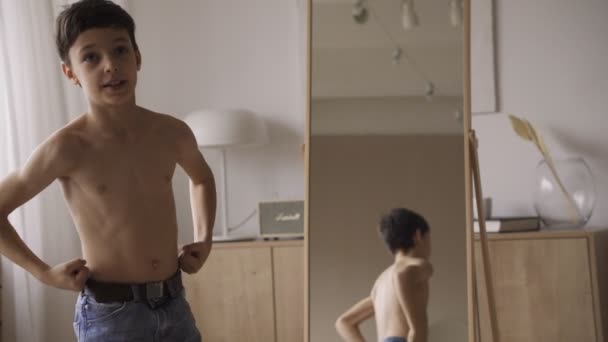 Niedlichen kaukasischen Jungen zeigt Muskeln vor dem Spiegel, Sport-Power, Gesundheit. — Stockvideo