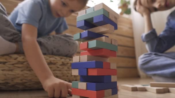 二人の兄弟は床に座っている木製のブロックから塔を構築しています。 — ストック動画
