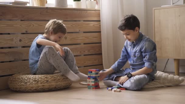 Twee broers bouwen een toren van houten blokken op de vloer. — Stockvideo