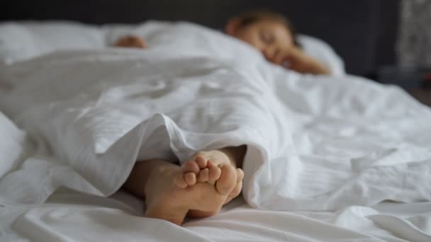 Frauenfüße auf dem Bett unter einer weißen Decke. Schlaf- und Relaxkonzept. Urlaub und Feiertagsthema. — Stockvideo