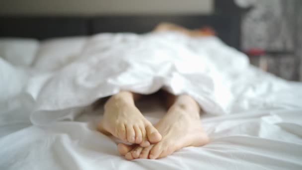 女性足白い毛布の下のベッドの上。睡眠とコンセプトをリラックスします。休暇や休日のテーマ. — ストック動画