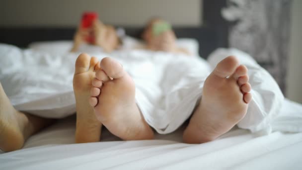 Tiro de pés namorado e namorada deitado na cama sob cobertor . — Vídeo de Stock