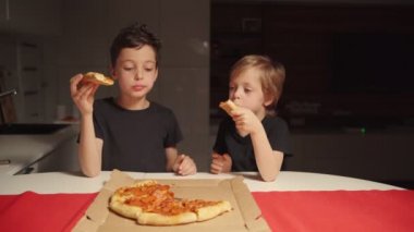 İki çocuk gece geç saatte evde pizza yiyorlar. Çocuklar evde yalnızlar..