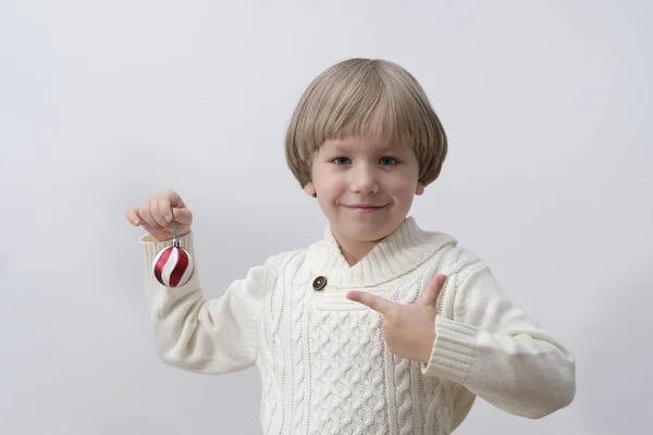 Kind met kerstversiering in de hand. Jongen op witte achtergrond. Nieuwjaars- en kerstconcept. — Stockfoto