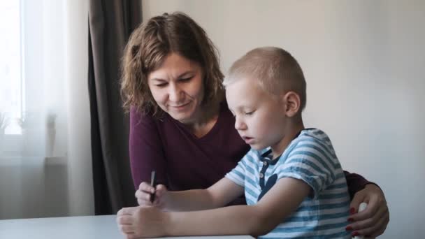 Ребенок сидит за столом дома и рисует вместе со своей мамой. Семейная концепция — стоковое видео