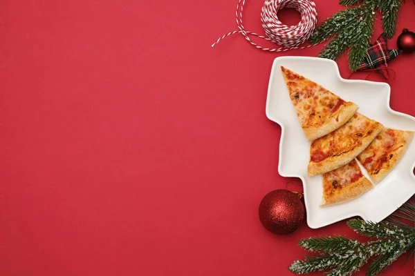 Dostawa pizzy na Gwiazdkę. Jadalne choinki wykonane z pizzy margarita na czerwonym tle z dekoracjami — Zdjęcie stockowe