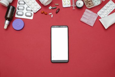 İnternette eczane ve eczane kavramı. Kırmızı arka planda ilaç hapları ve akıllı telefon, metin için boşluk