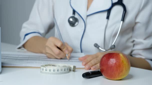 Médica nutricionista preenchendo plano de dieta em uma mesa, close-up — Vídeo de Stock