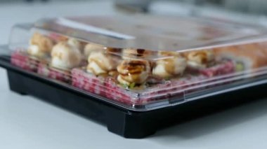 Delivery food concept: woman opening plastic box with sushi rolls