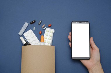 İnternette eczane ve eczane kavramı. Kese kağıdında ilaç hapları ve mavi arka planda akıllı telefon, mesaj için yer