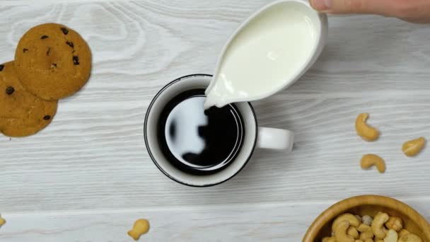 Hand toevoegen van melk aan koffie in een kopje op houten tafel, bovenaanzicht — Stockvideo
