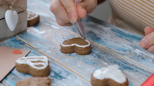 Жінка прикрашає імбирне печиво у формі серця на день Святого Валентина або Різдво, покриваючись білою глазур'ю, крупним планом — стокове відео