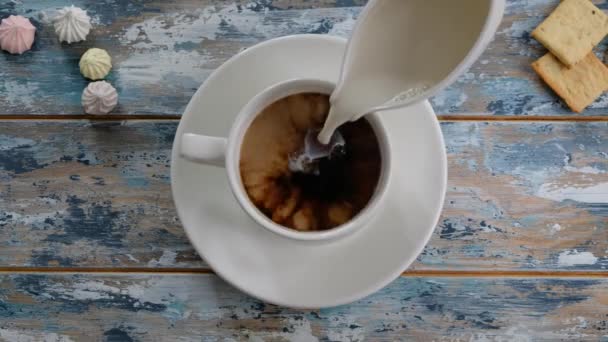 Рука добавления молока к кофе в чашку на деревянный стол, вид сверху — стоковое видео