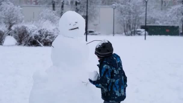 Child with snowman in winter snowy day, christmas holidays — Stock Video
