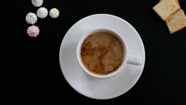 Añadir leche a mano al café y revolver el café en una taza en la mesa negra, vista superior — Vídeo de stock