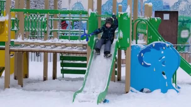 Niño jugando en los niños se deslizan en invierno en el patio de recreo, feliz de la primera nieve — Vídeos de Stock