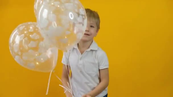 Feliz niño pequeño bailando con globos sobre un fondo amarillo aislado — Vídeo de stock