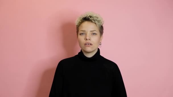 Glimlachende stijlvolle vrouw geheim te houden en te kijken naar de camera over roze achtergrond — Stockvideo