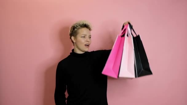 Stijlvolle jonge vrouw met boodschappentassen geïsoleerd over roze achtergrond. Winkelen en verkoop concept. — Stockvideo