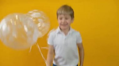 Sarı arka planda balonlarla dans eden mutlu küçük çocuk.