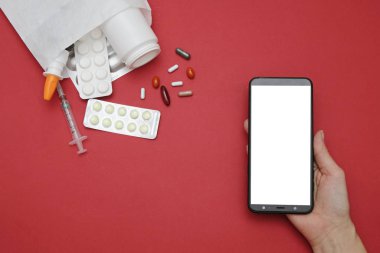 İnternette eczane ve eczane kavramı. Kırmızı arka planda ilaç hapları ve akıllı telefon, metin için boşluk