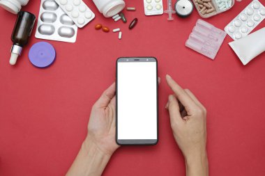 İnternette eczane ve eczane kavramı. İlaç hapları ve akıllı telefon kırmızı arka planda, mesaj için boşluk