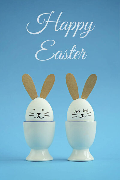 Blue Easter background - two white eggs decorated like rabbits. Greeting card