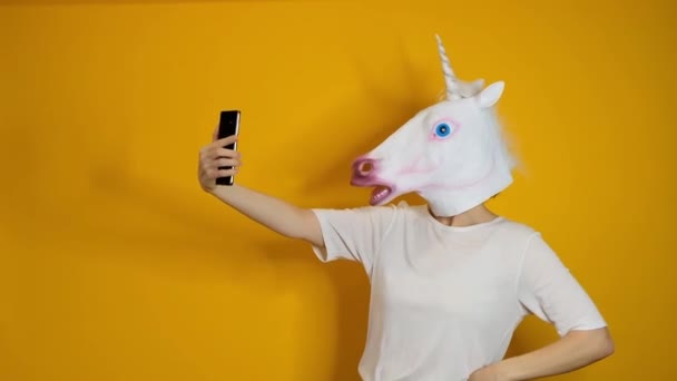 Extraño vídeo divertido - mujer con cabeza de unicornio haciendo selfie con teléfono inteligente sobre fondo amarillo — Vídeos de Stock