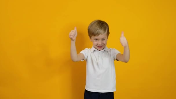 Klein glimlachend vijf jaar oud jongen tonen duim omhoog over gele achtergrond — Stockvideo