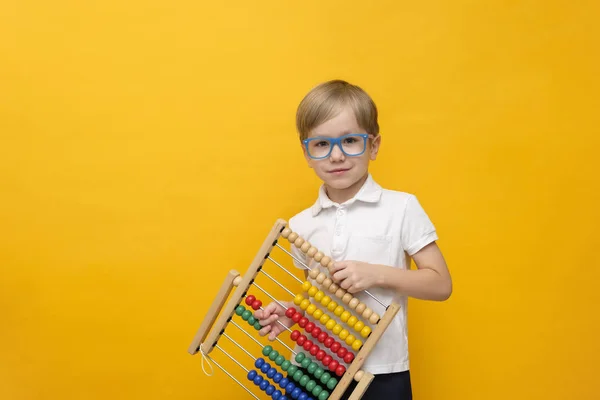 Cute little school boy in glasses holding scores on yellow background, copy space. Math concept — 스톡 사진