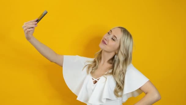 Piękna blondynka robi selfie na smartfonie na żółtym tle — Wideo stockowe