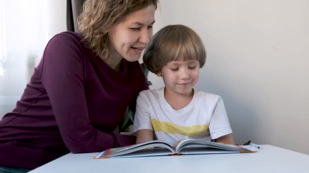 Anaokulu çocuğu, çocuk, evde masada oturup annesiyle kitap okuyor. — Stok video