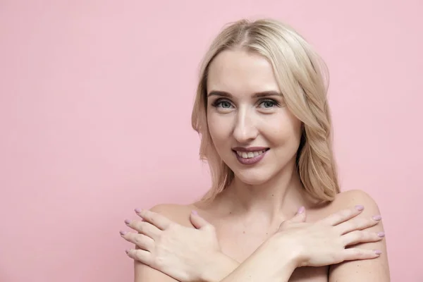 Pastel pembe arka planda çıplak omuzlu güzel sarışın kadın. Güzellik, kozmetik ve cilt bakım konsepti