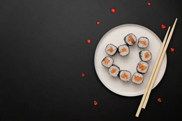 Sevgililer Günü için suşi - kalp şeklinde yuvarlan, siyah arka planda tabak üzerinde. Düz yatıyordu. Metin için boşluk.