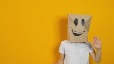 Kafasında torbayla dans eden küçük bir çocuk. Sarı arka planda gülümseyen bir yüzle.