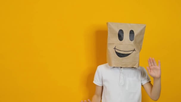 Niño pequeño con una bolsa en la cabeza bailando con la cara sonriente feliz sobre fondo amarillo — Vídeos de Stock