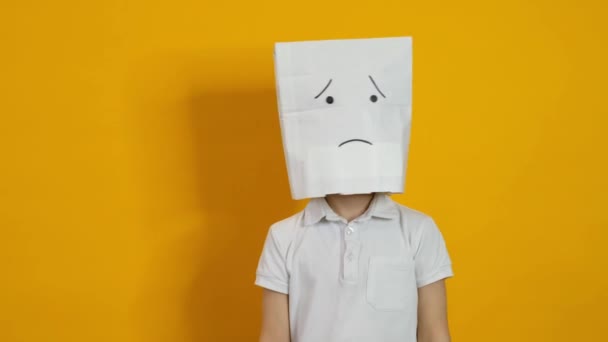Kleine jongen met een zak op zijn hoofd - triest, teleurgesteld gezicht op gele achtergrond — Stockvideo