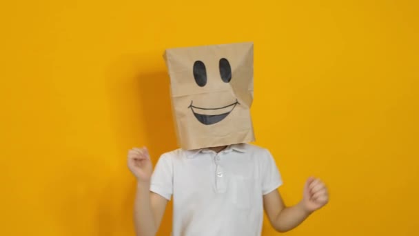 Menino com um saco na cabeça dançando com o rosto sorridente feliz no fundo amarelo — Vídeo de Stock