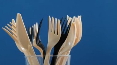 Plastic forks, knifes in glass, blue background. Concept of Recycling plastic and ecology problem