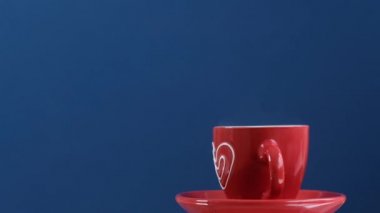 Red cup of hot coffee with heart rotating on blue background