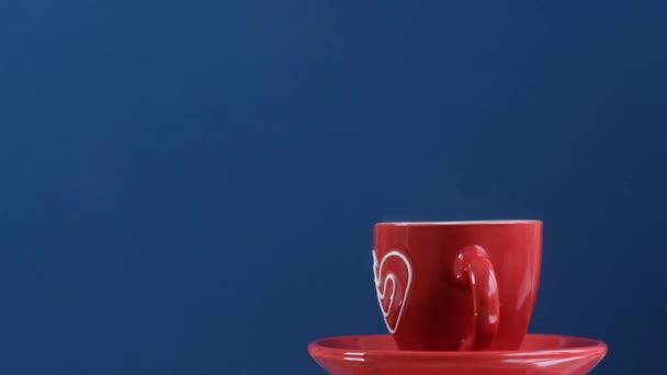Red cup of hot coffee with heart rotating on blue background — 图库视频影像