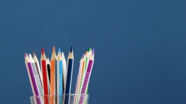 Colorful pencils rotating in glass, blue background. Back to school concept
