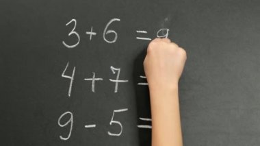 Kara tebeşir tahtasında basit matematik alıştırmaları yapan çocuk el, kapat.