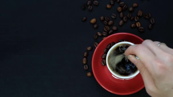 Dark coffee in red cup and coffee beans on black table with copy space. Top view — Stock videók