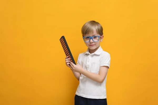 Roztomilý malý školák v brýlích, držící Atakus na žlutém pozadí. Duševní aritmetika, matematika, matematika — Stock fotografie